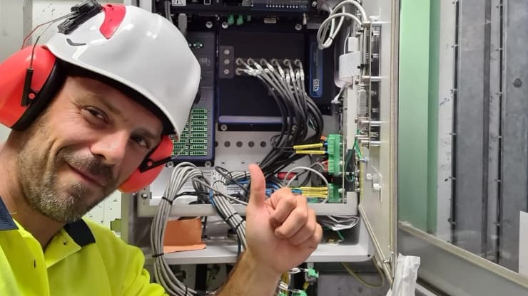 Técnico de servicio de Qualitrol con casco y protección auditiva trabajando en panel de control eléctrico